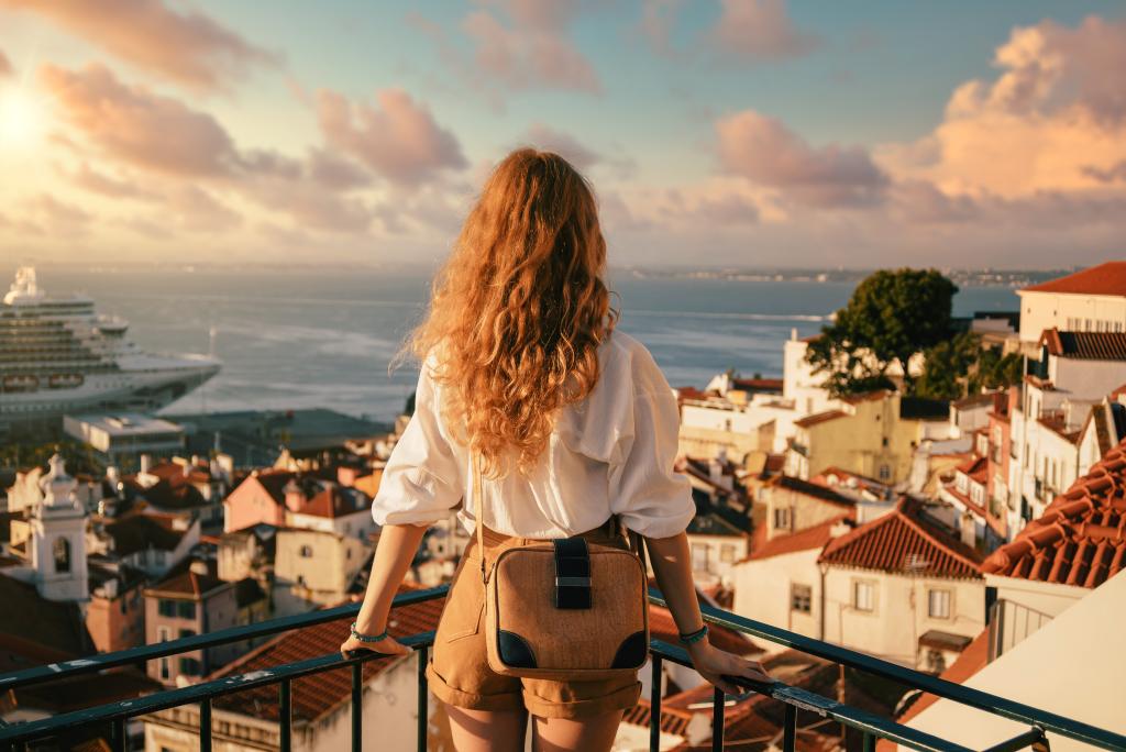 young-female-standing-on-a-platform-surrounded-by-fences-and-observing-lisbon-at-daytime-in-portugal.jpg